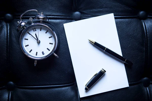 Alarm clock and pen and paper on black leather — Stock Photo, Image