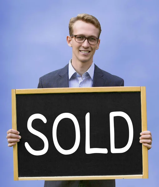 Młody człowiek posiadający znak z napisem sprzedane — Zdjęcie stockowe