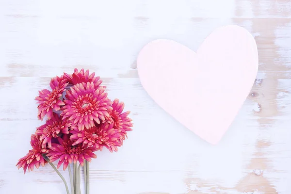 Red flowers and wooden heart on white table — Stock Photo, Image