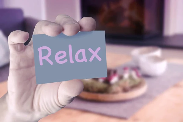 Mão na frente da sala de estar segurando cartão com a palavra Relaxe — Fotografia de Stock