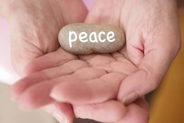 Nærme seg av kvinners hender og holde stein med ordet fred – stockfoto