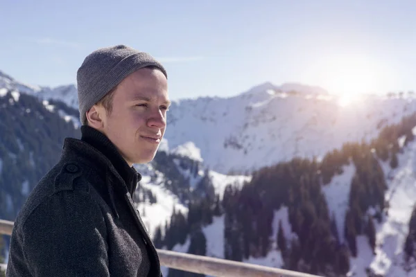 Young man standing in the sun surrounded by snowy mountains — Stock Photo, Image