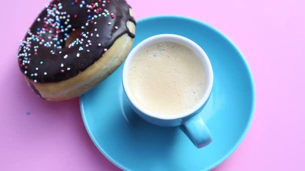 Taza de café azul con rosquilla de chocolate en el plato rosado giratorio — Vídeos de Stock