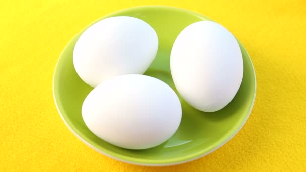 Three raw eggs on green rotating plate on yellow table — Stock Video