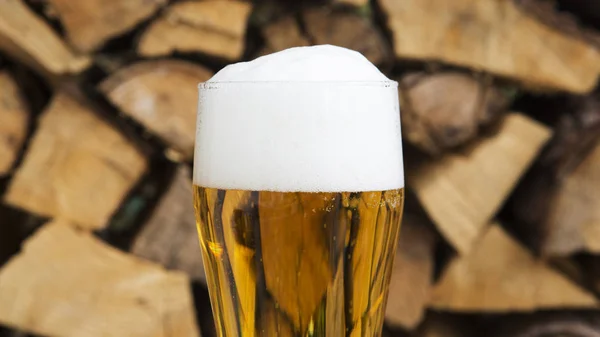 Glass of beer with froth in front of firewood — Stock Photo, Image