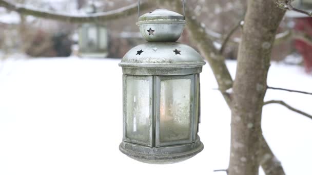 Фонарь со свечой, висящей на дереве в саду на снегу — стоковое видео