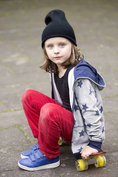 Мальчик в шляпе, сидящий на скейтборде — стоковое фото