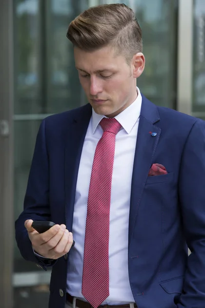 Schöner blonder Mann im Anzug, der draußen mit seinem Handy steht — Stockfoto