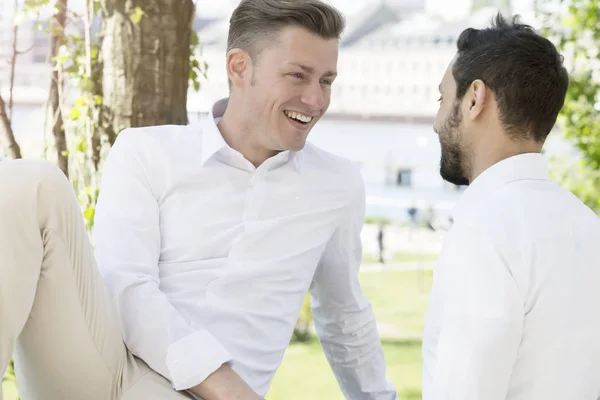 Two young man sitting outside at park and smiling at each other — Stock Photo, Image