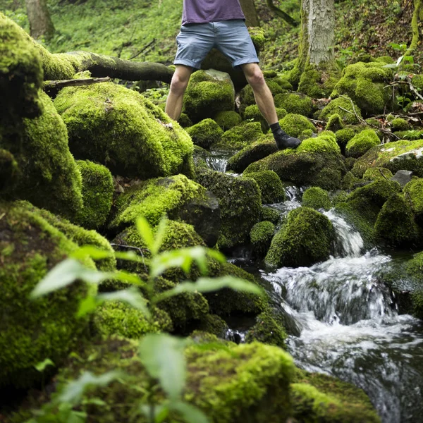 Jovem atravessando um riacho na floresta verde — Fotografia de Stock