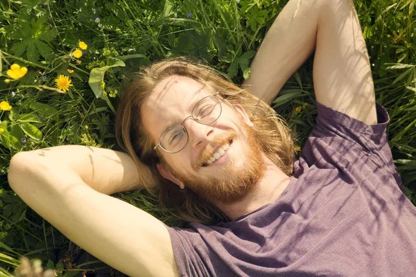 红头发的年轻男子躺在草丛中和微笑 — 图库照片