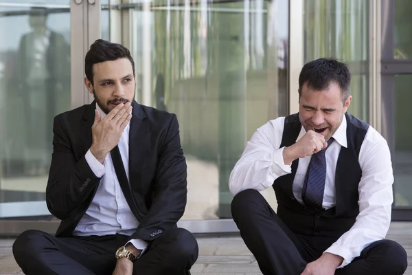 Dois empresários sentados do lado de fora e bocejando — Fotografia de Stock