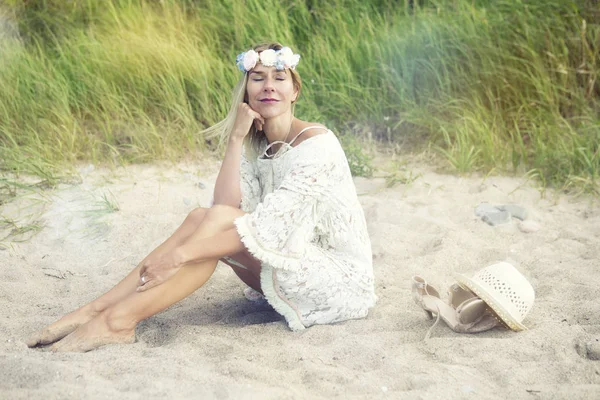 Mujer rubia en vestido blanco sentada en la playa — Foto de Stock