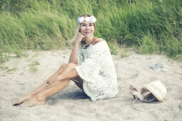 Mujer rubia en vestido blanco sentada en la playa — Foto de Stock