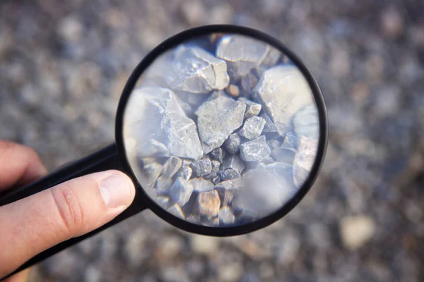 Рука держит увеличительное стекло на камнях — стоковое фото