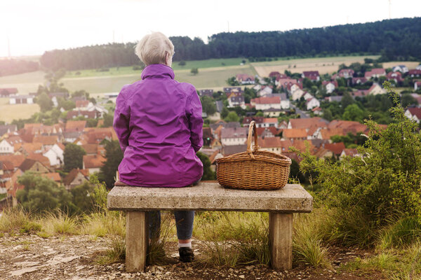 older woman sitting on bench and looking at small town