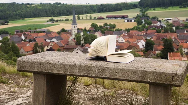 在一张石凳与小镇的看法上的书 — 图库照片