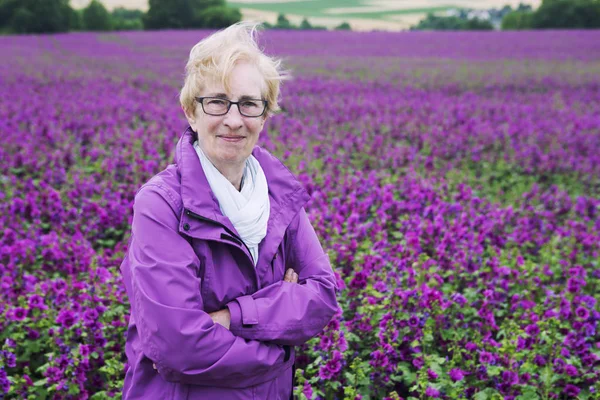 Woman in front of flower field smiling at camera — Stock Photo, Image
