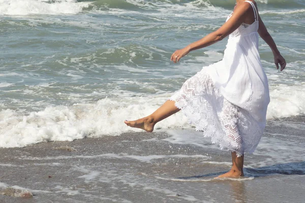 Femme en robe blanche marchant pieds nus le long de la plage — Photo