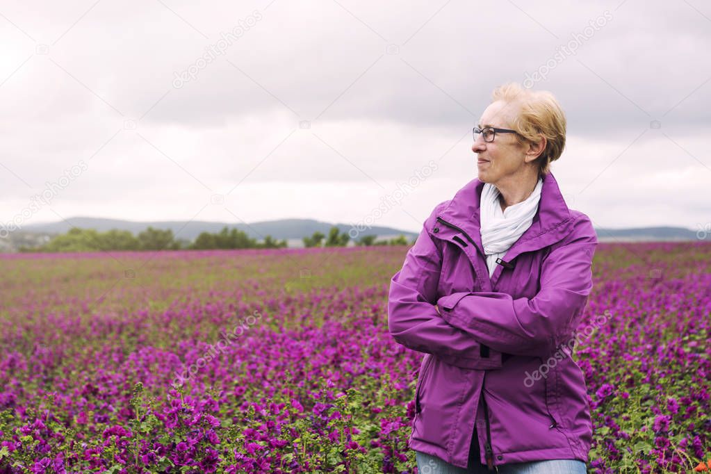 older woman standing at field of purple flowers and enjoying the