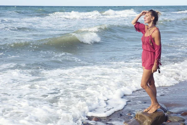 Mulher loira em vestido vermelho em pé junto ao oceano — Fotografia de Stock