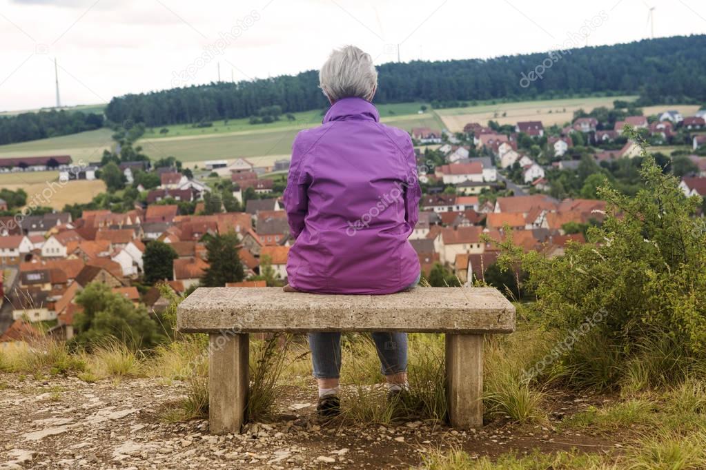 older woman sitting on bench and looking at town