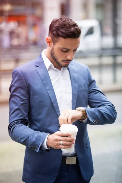 Business man looking at his watch and holding a cup — стоковое фото