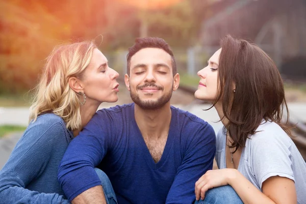 two beautiful women kissing man on his cheeks