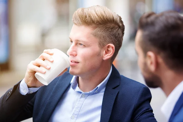 Zwei Geschäftsleute draußen, während einer aus einer Tasse trinkt — Stockfoto