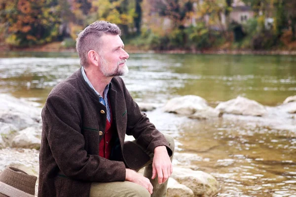 Bávaro homem em seus 50 anos sentado à beira do rio — Fotografia de Stock