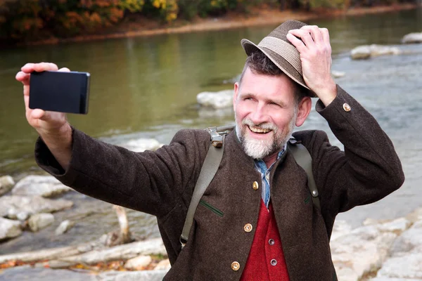 Bávaro homem em seus 50 anos de pé à beira do rio e tomar uma selfie — Fotografia de Stock