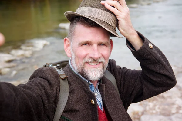 Bavarian man in his 50s standing by river and taking a selfie — Stock Photo, Image