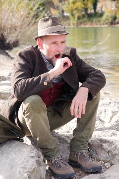 Баварский человек, сидящий у реки и зевающий — стоковое фото