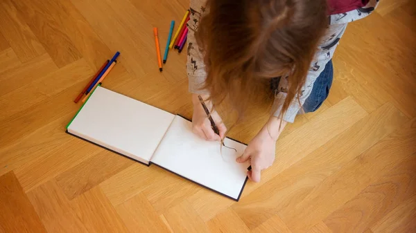 Criança sentada no chão e desenho em caderno — Fotografia de Stock