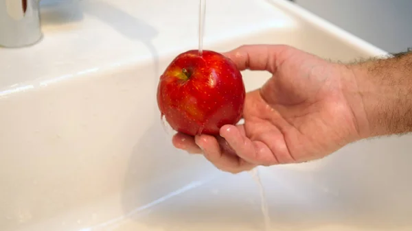 Mão lavando uma maçã vermelha na pia — Fotografia de Stock