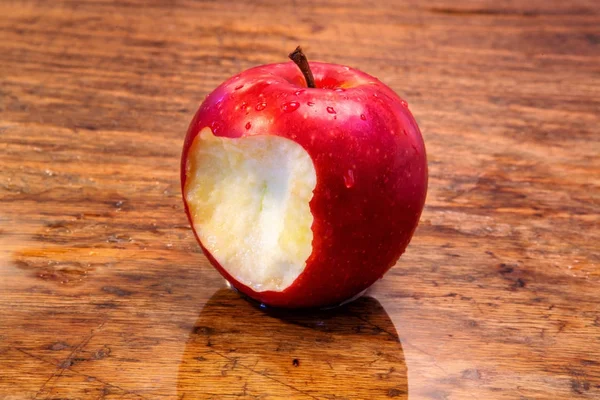 Красное мокрое яблоко с укусом на деревенском деревянном столе — стоковое фото
