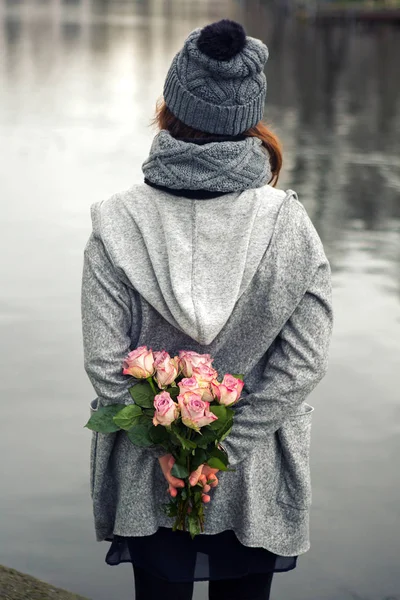 Ung kvinna som står vid vattnet med bukett rosor — Stockfoto