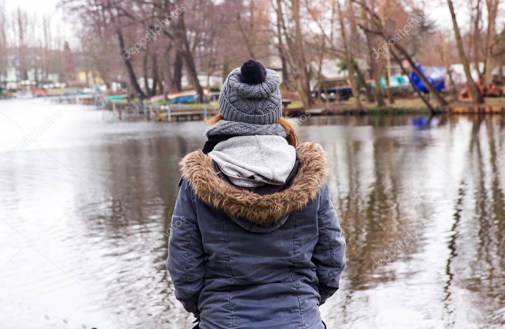 young woman in coat standing by the water in the cold