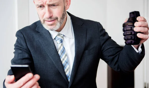 Sconvolto uomo d'affari guardando il telefono e tenendo una granata a mano — Foto Stock