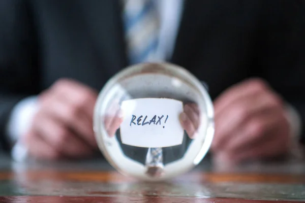 Homem segurando papel com a palavra Relaxe na frente da bola de vidro — Fotografia de Stock