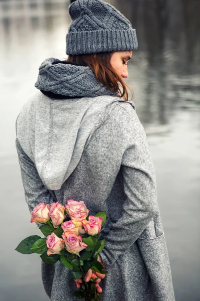 Jovem mulher em pé junto à água com buquê de rosas — Fotografia de Stock