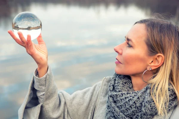 Donna di fronte al lago regge una palla di vetro — Foto Stock
