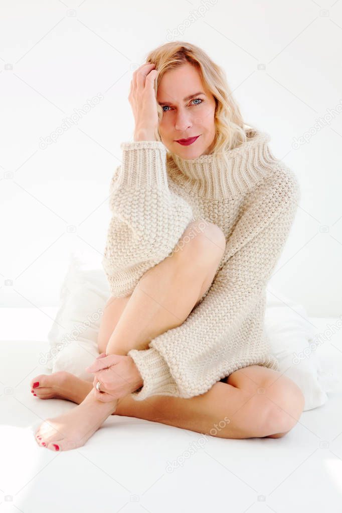 portrait of blond woman in beige sweater sitting in bed
