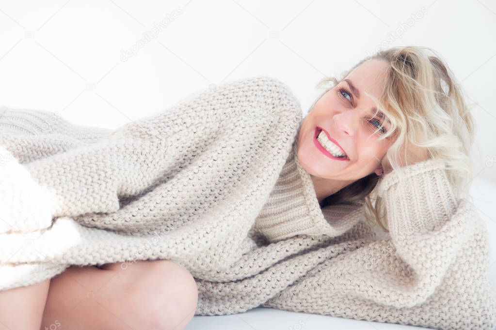 portrait of blond woman in beige sweater lying in bed