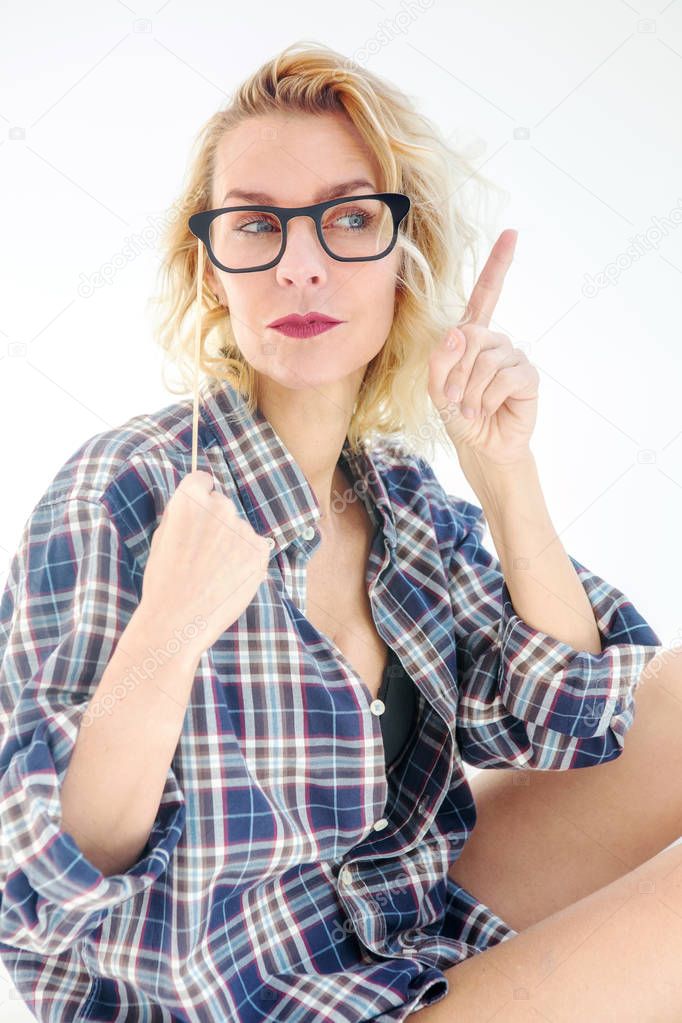 blond woman in shirt sitting in bed and holding glasses to her f