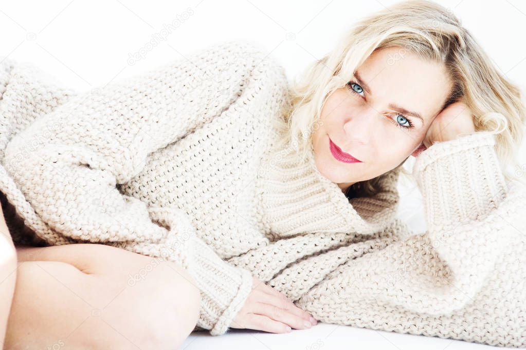 beautiful blond woman in beige sweater lying in bed