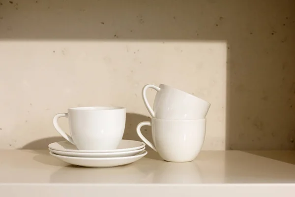 Weiße Keramiktassen und Untertasse im Regal — Stockfoto