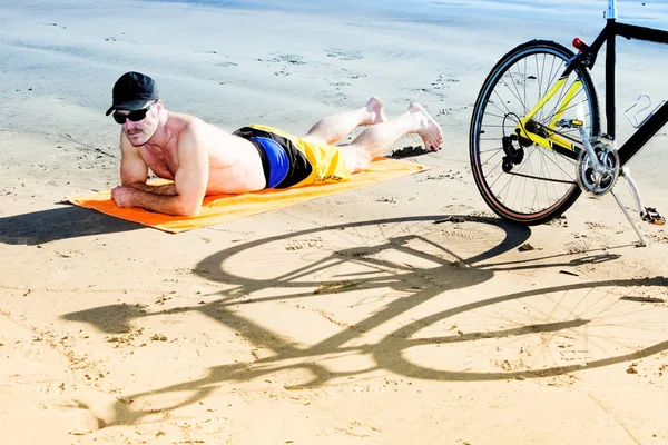 Homem bonito deitado na praia ao lado de sua bicicleta — Fotografia de Stock