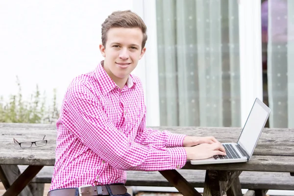 Bello giovane seduto all'aperto con il suo computer portatile — Foto Stock