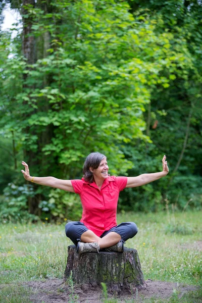 Femme heureuse dans sa cinquantaine assis sur une souche d'arbre — Photo